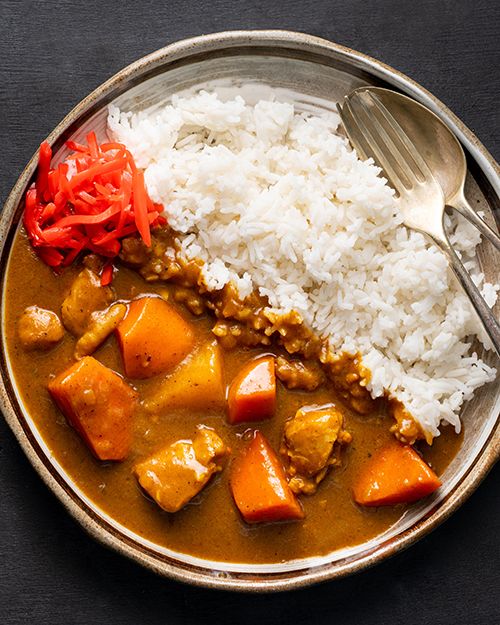 a bowl filled with rice, meat and vegetables next to a spoon on top of a table