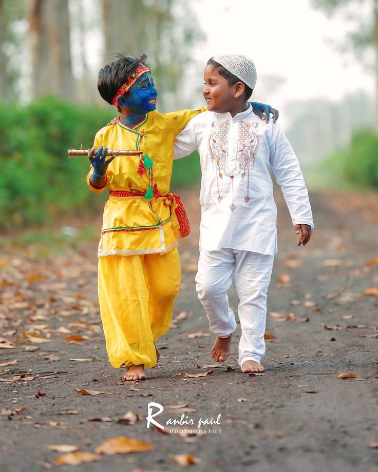 two young boys dressed in colorful costumes walking down a dirt road holding hands with each other