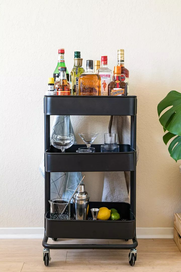 a bar cart with drinks on it next to a potted plant and other items