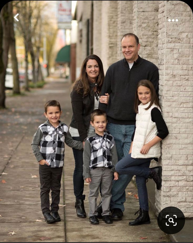 a family poses in front of a brick wall on the sidewalk with their two children