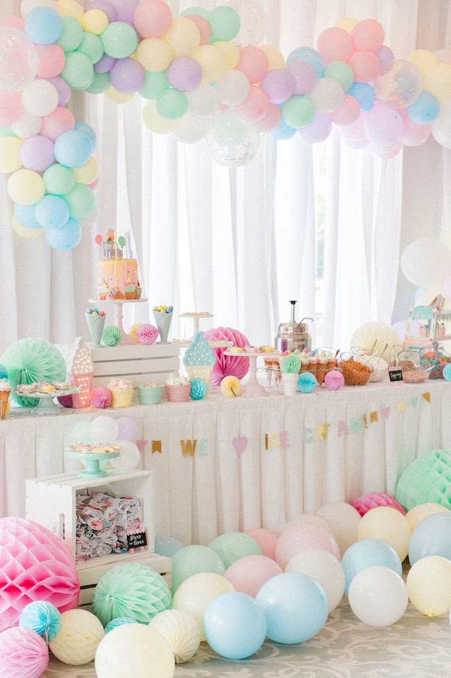 a party with balloons, cake and other items on the table in pastel colors