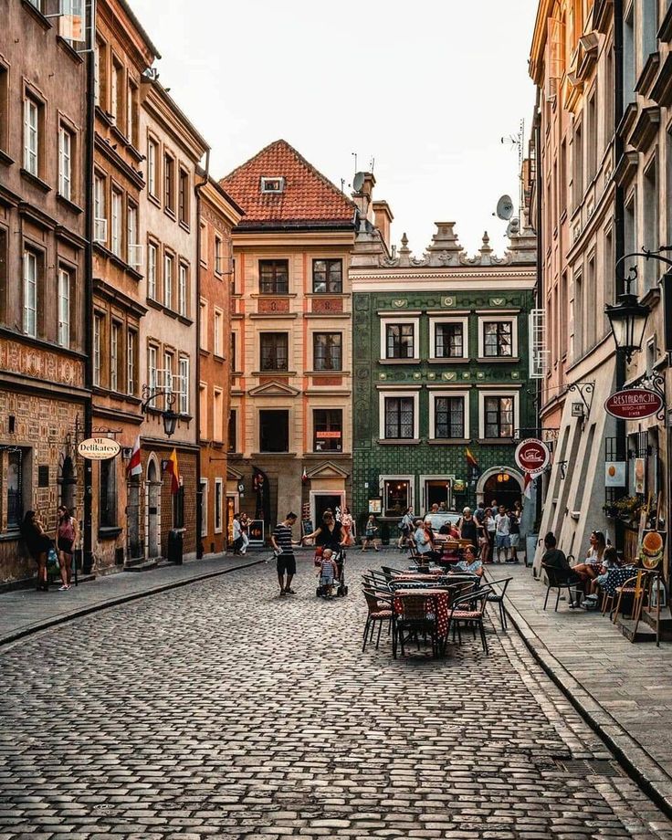 an old cobblestone street with tables and chairs in the middle, surrounded by tall buildings