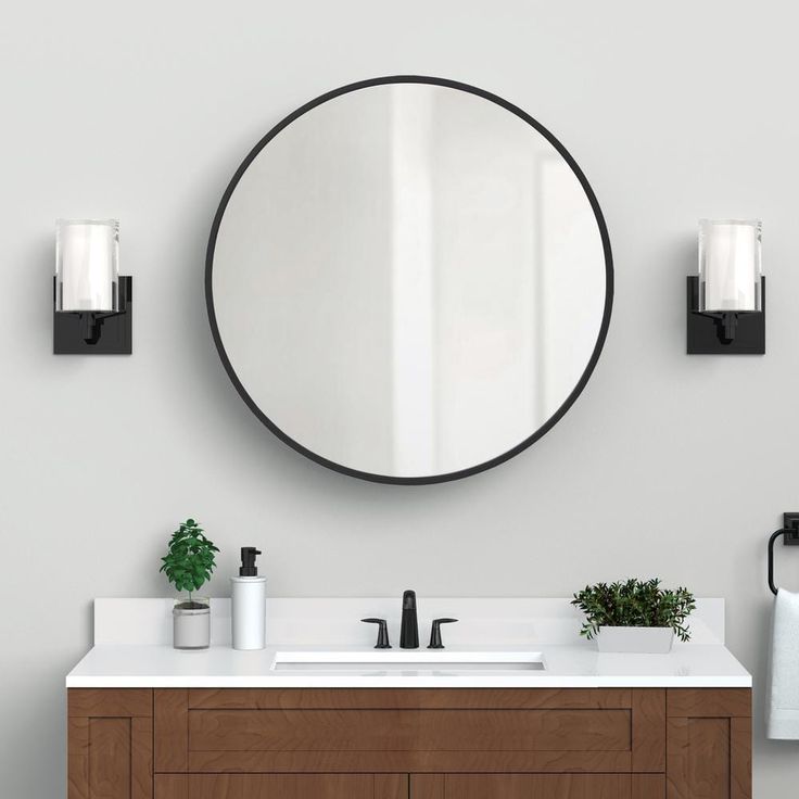 a bathroom vanity with a round mirror above it and two candles on the wall next to it