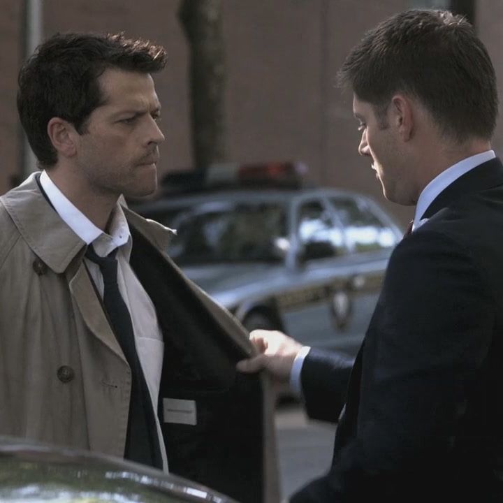 two men standing next to each other in front of a car and one is shaking hands with the other man