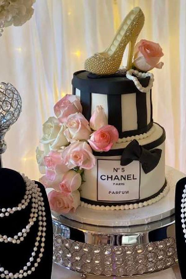 a black and white cake with pink roses on top, pearls around the neck and high heel shoes