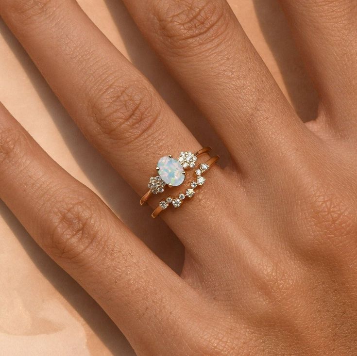 a woman's hand with two rings on it, one has a heart shaped diamond and the other has an opal