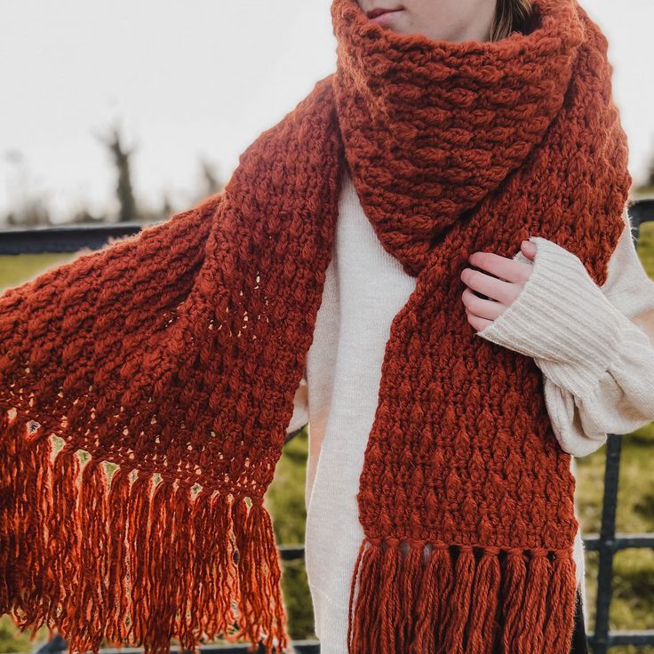 a woman standing in front of a metal fence wearing a red knitted shawl