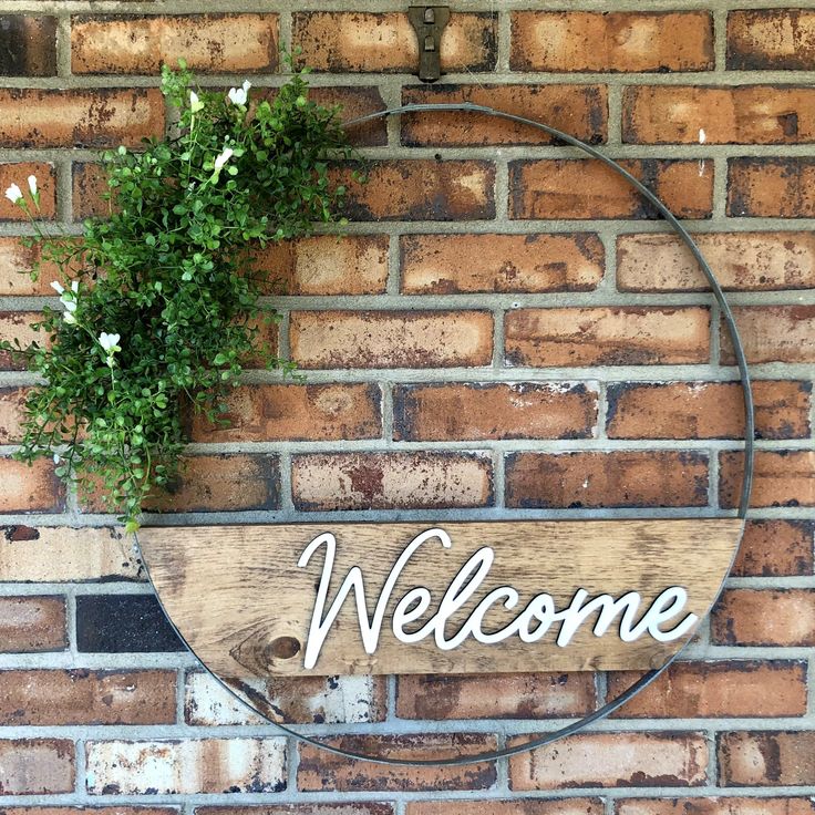 a welcome sign hanging on the side of a brick wall next to a potted plant