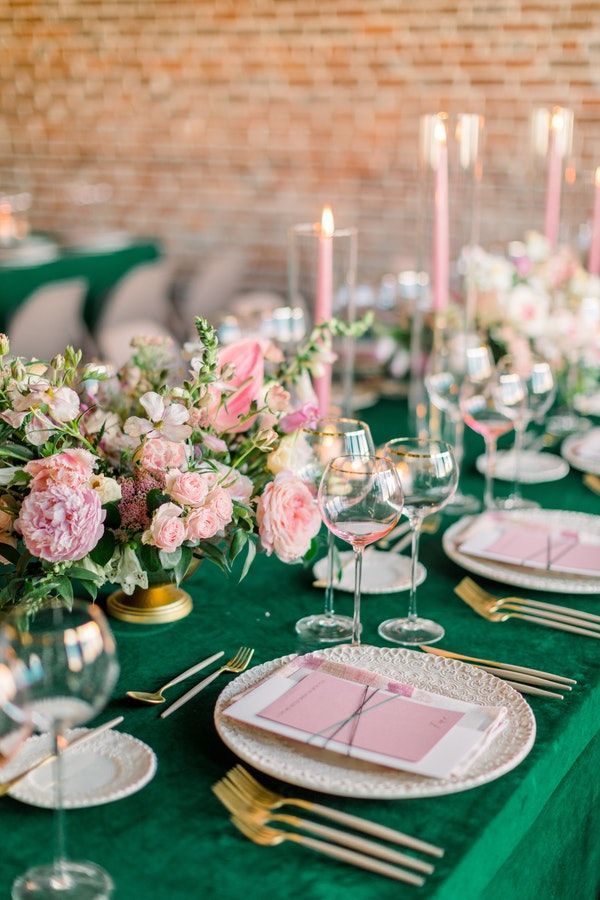 a table set with plates, silverware and pink flowers on green cloth covered tables