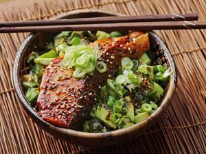 a bowl filled with meat and vegetables on top of a bamboo table next to chopsticks