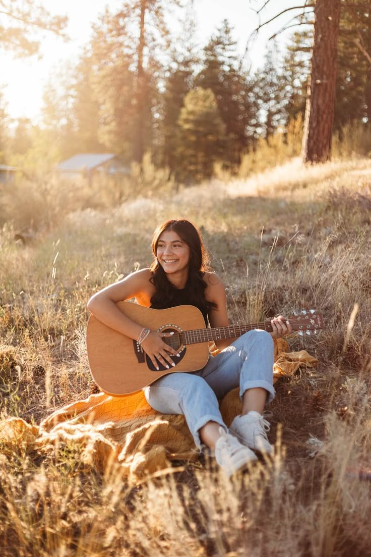 a woman sitting in the grass with her guitar