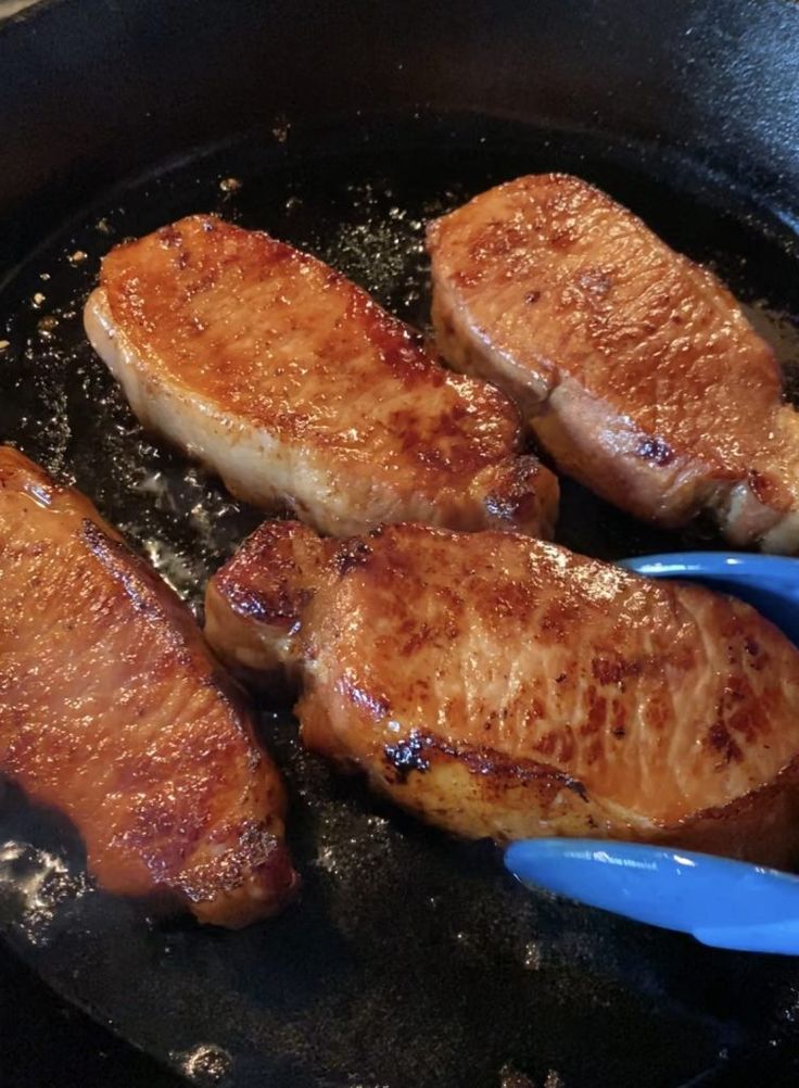 four pieces of meat being cooked in a skillet