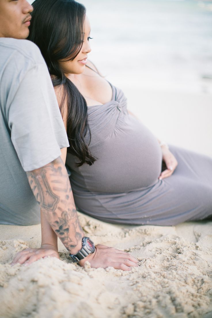 a pregnant woman sitting on the beach next to a man