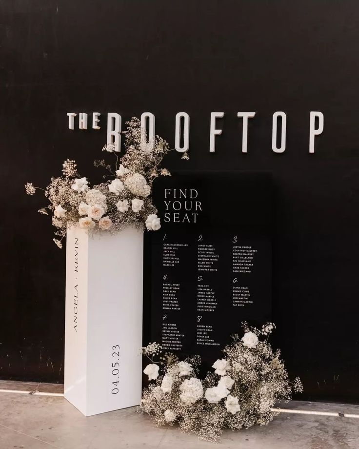 a white vase filled with flowers sitting next to a black and white sign that says the booth