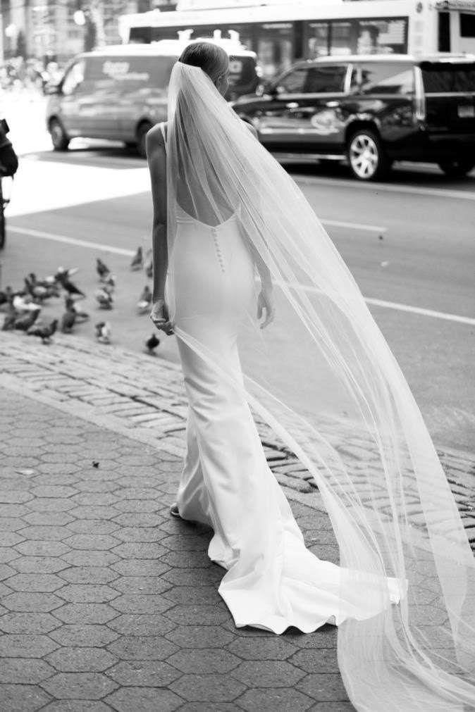 the bride is walking down the street with her veil blowing in the wind and pigeons on the sidewalk