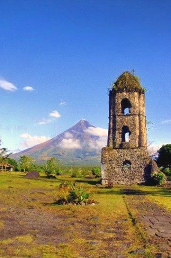 an old stone tower in the middle of a field with mountains in the back ground