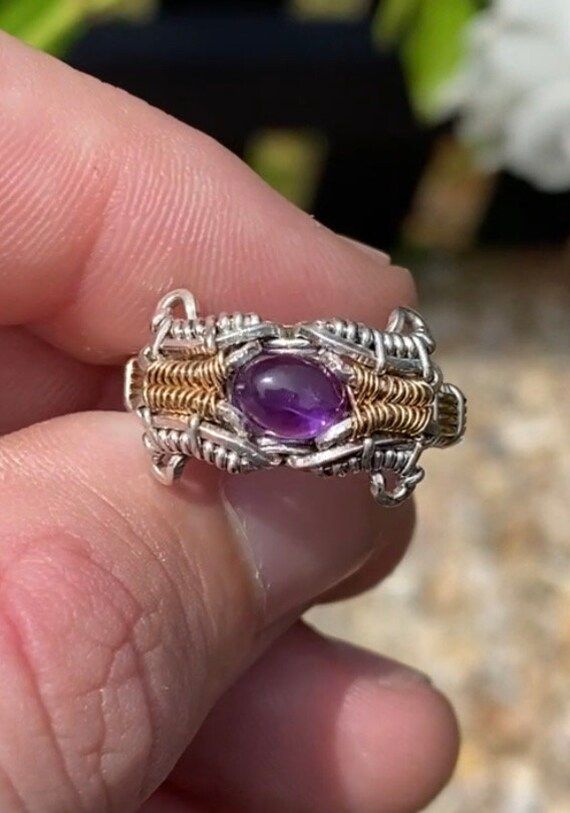 This size 7 ring features a stunning amethyst and peridot gemstone with an intricate pattern woven along the band. Spun in .925 silver and 14k yellow gold fill wire. Includes complimentary polishing pad and gift box. Artisan Hand Wrapped Oval Jewelry, Artisan Oval Hand-wrapped Jewelry, Purple Hand Wrapped Bohemian Jewelry, Purple Bohemian Hand Wrapped Jewelry, Purple Bohemian Hand-wrapped Jewelry, Handmade Oval Dainty Jewelry, Handmade Spiritual Ring Jewelry, Artisan Sterling Silver Jewelry In Purple, Artisan Sterling Silver Purple Jewelry