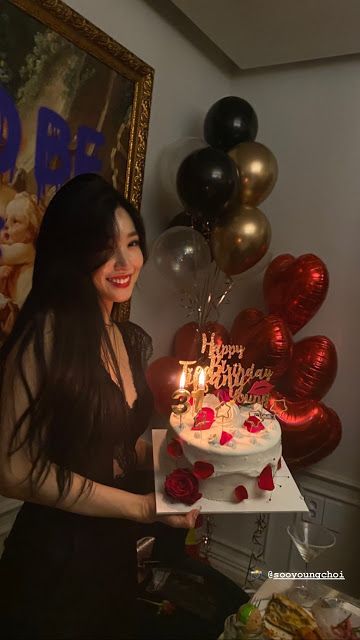 a woman is holding a birthday cake with candles on it and balloons in the background