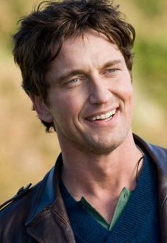 a close up of a person wearing a leather jacket and smiling at the camera with grass in the background