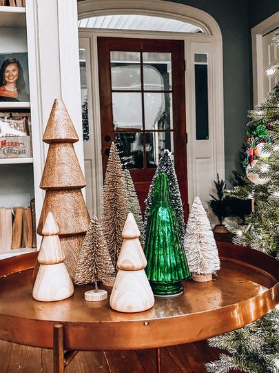 three christmas trees sitting on top of a wooden table in front of a book shelf