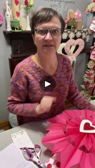 a woman sitting at a table with pink paper flowers and scissors in front of her