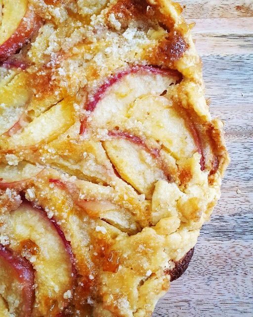 an apple pie with crumbs on top sitting on a wooden table next to a fork