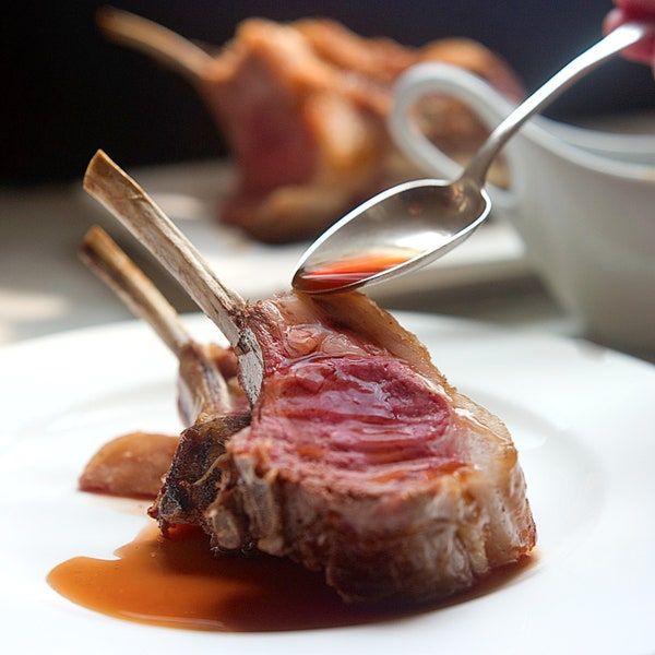 a piece of meat on a white plate with a fork in it and sauce being drizzled over the top