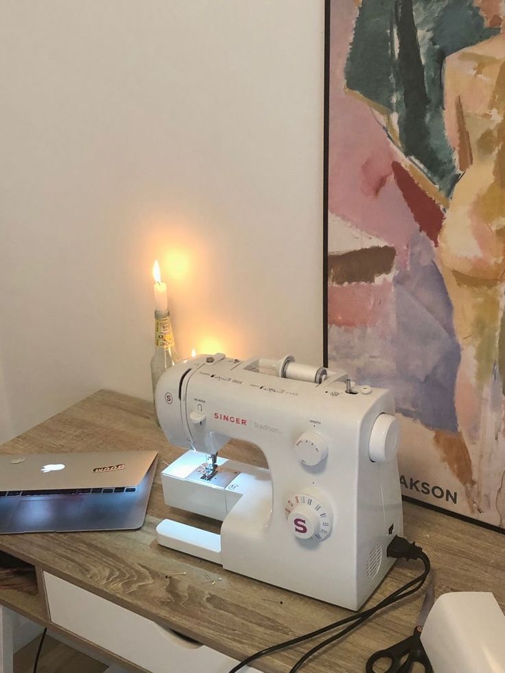 a white sewing machine sitting on top of a wooden table next to a lit candle