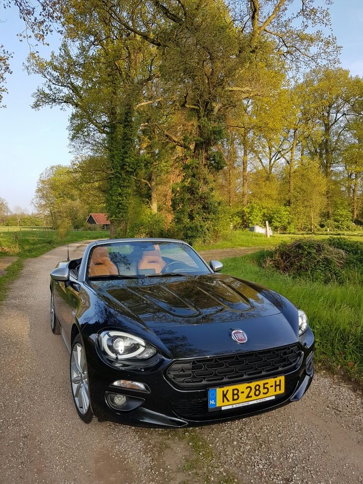 a black sports car parked on the side of a dirt road next to grass and trees