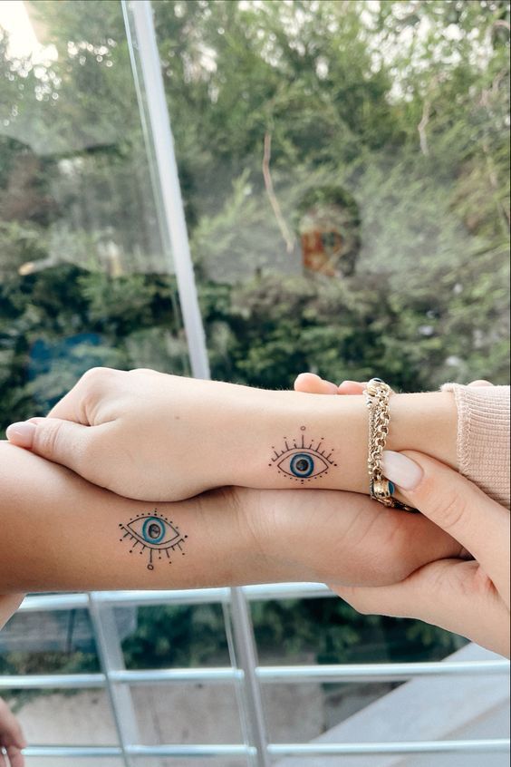 two people holding each other's hands with tattoos on their fingers and eye tattoo