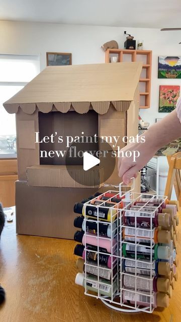 a cat sitting on the floor next to a cardboard house