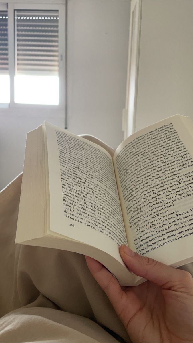 a person is reading a book while laying in bed with their hand on the open book