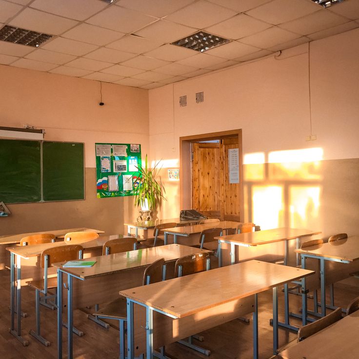 an empty classroom with wooden desks and green chalkboard