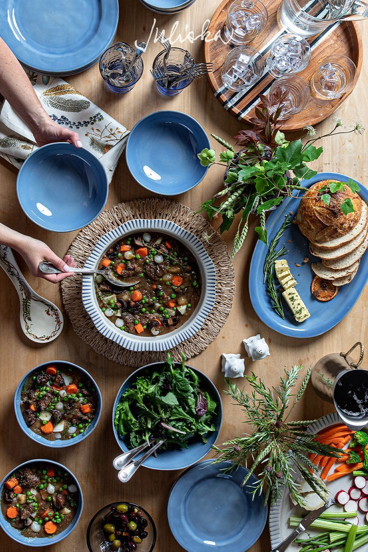 a table topped with blue plates and bowls filled with food next to utensils