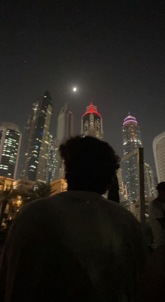 a man standing in front of a city skyline at night with buildings lit up behind him