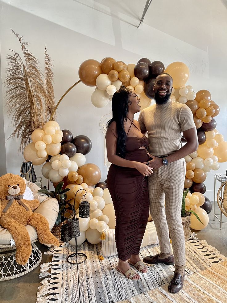 a man and woman standing next to each other in front of balloon arch with teddy bears