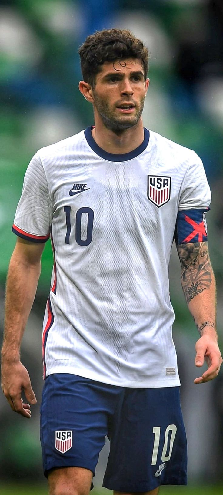 a soccer player with tattoos on his arm and chest, walking across the field during a game