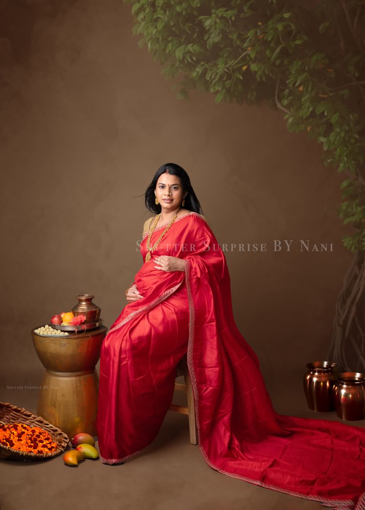 a woman in a red sari sitting on a chair next to a basket of fruit