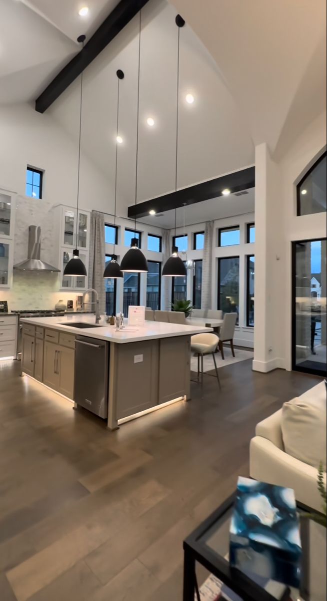 a large open concept kitchen and living room with wood flooring, high ceiling lighting, and white walls