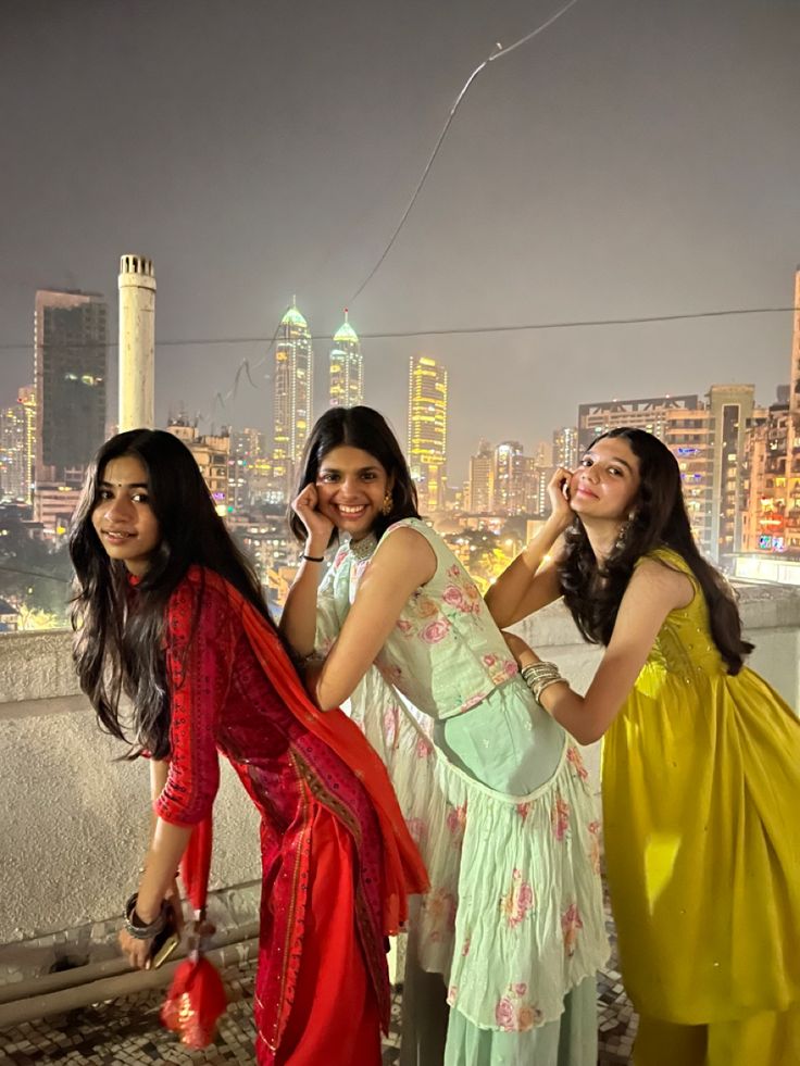 three young women standing on top of a roof in front of a cityscape