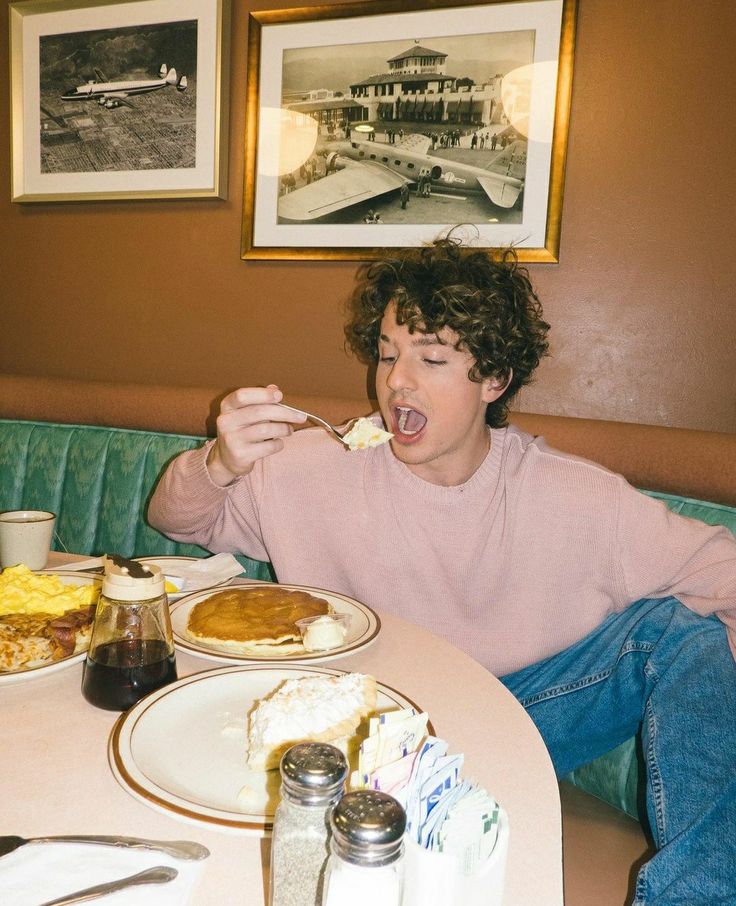 a young man sitting at a table eating food with his mouth open and tongue out