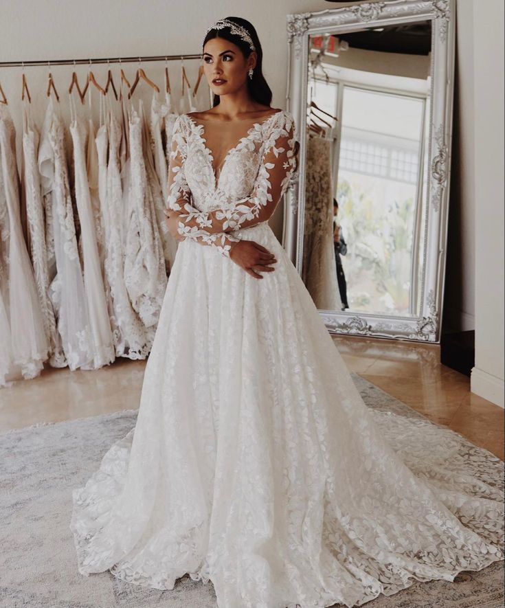 a woman standing in front of a mirror wearing a wedding dress with long sleeves and an open back