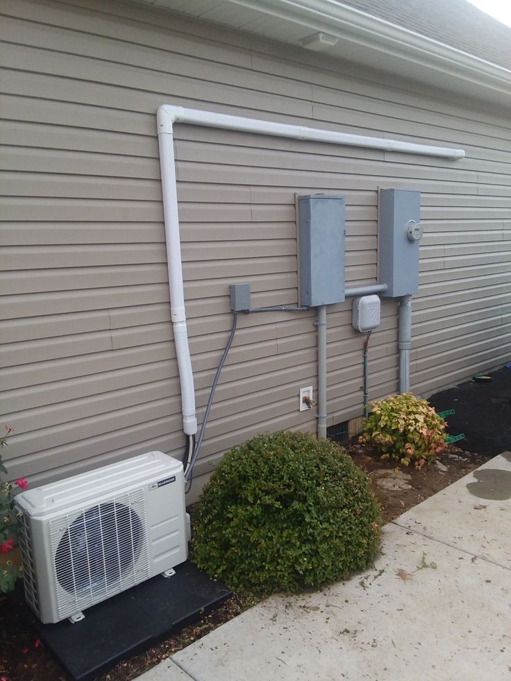 an air conditioner is attached to the side of a building next to a bush