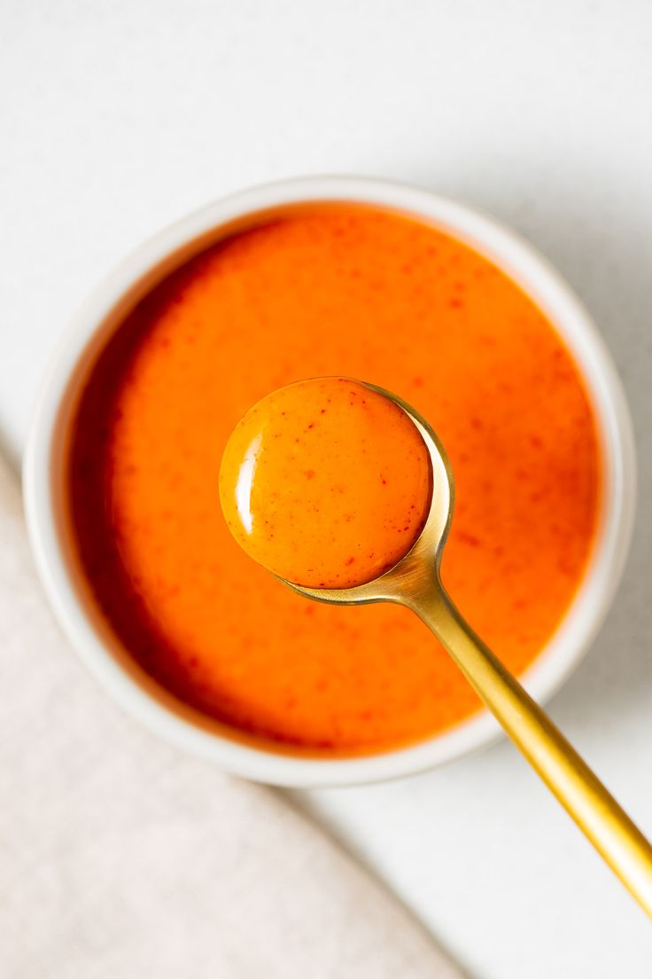 a spoon in a white bowl filled with tomato soup on a table top next to a napkin