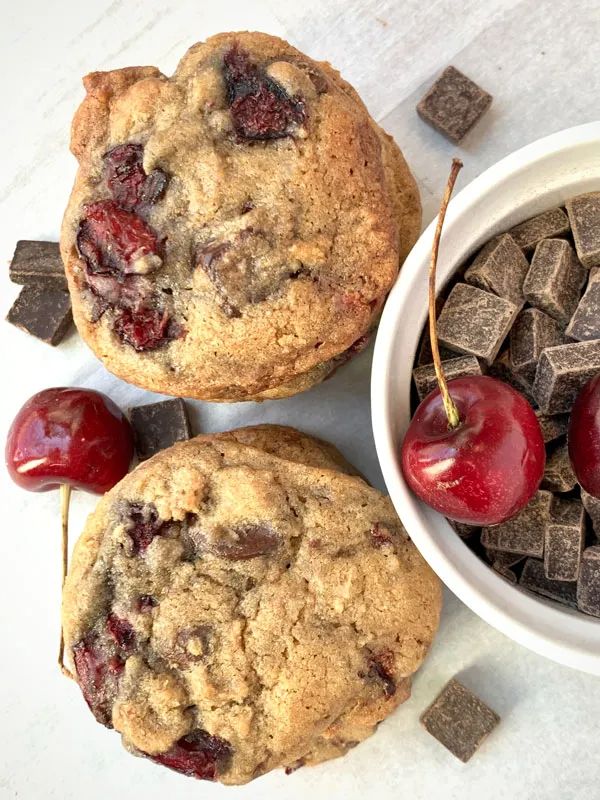 three cherries and two chocolate chip cookies on a table