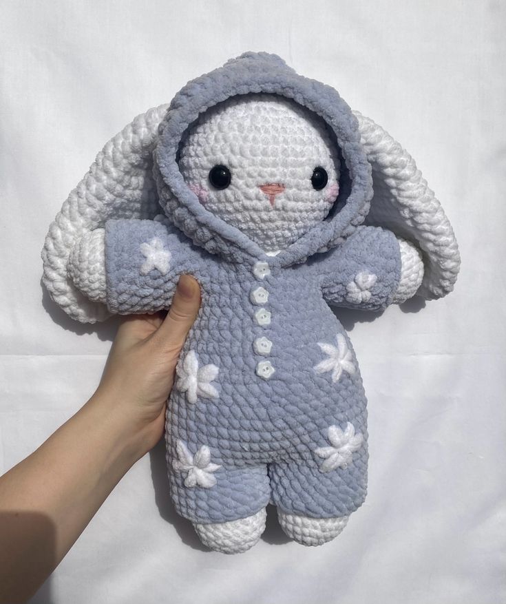 a crocheted stuffed animal is being held by a person's hand on a white sheet