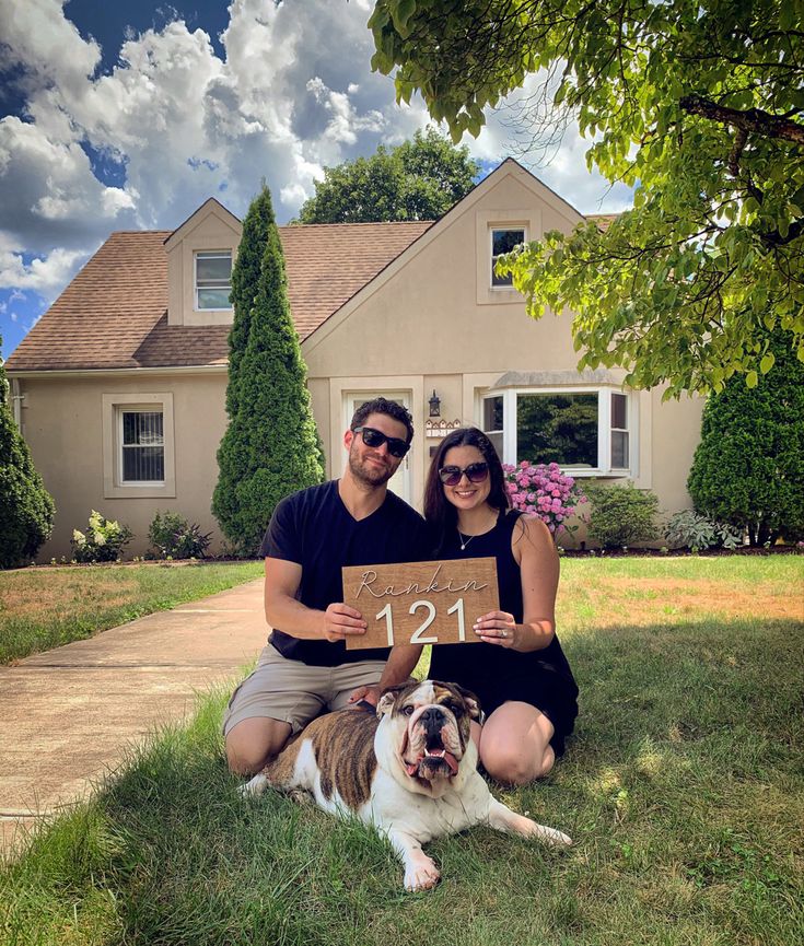 a man and woman sitting in front of a house with a dog on the lawn