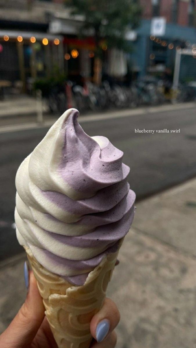 a hand holding an ice cream cone with purple frosting on it's top