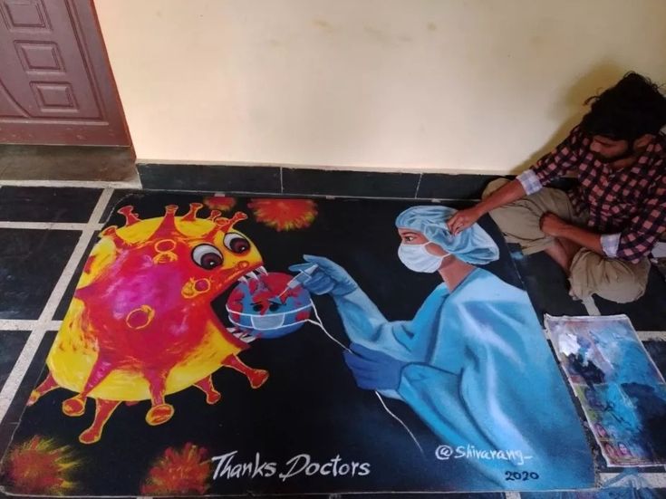 a man sitting on the floor next to a painting with an image of a person wearing a face mask