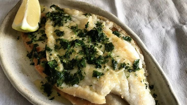 a white plate topped with fish covered in cheese and spinach next to a lemon wedge